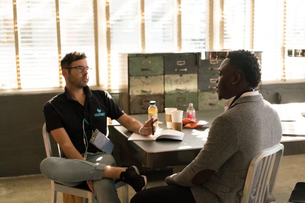 man wearing black polo shirt and gray pants sitting on white chair. Talk To Us campaign