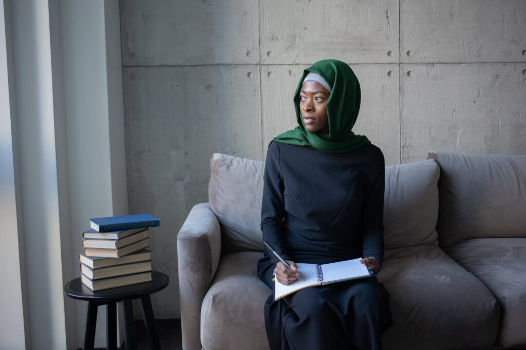 islamic african american female in hijab on sofa with notebook as we attempt to amplify marginalised voices