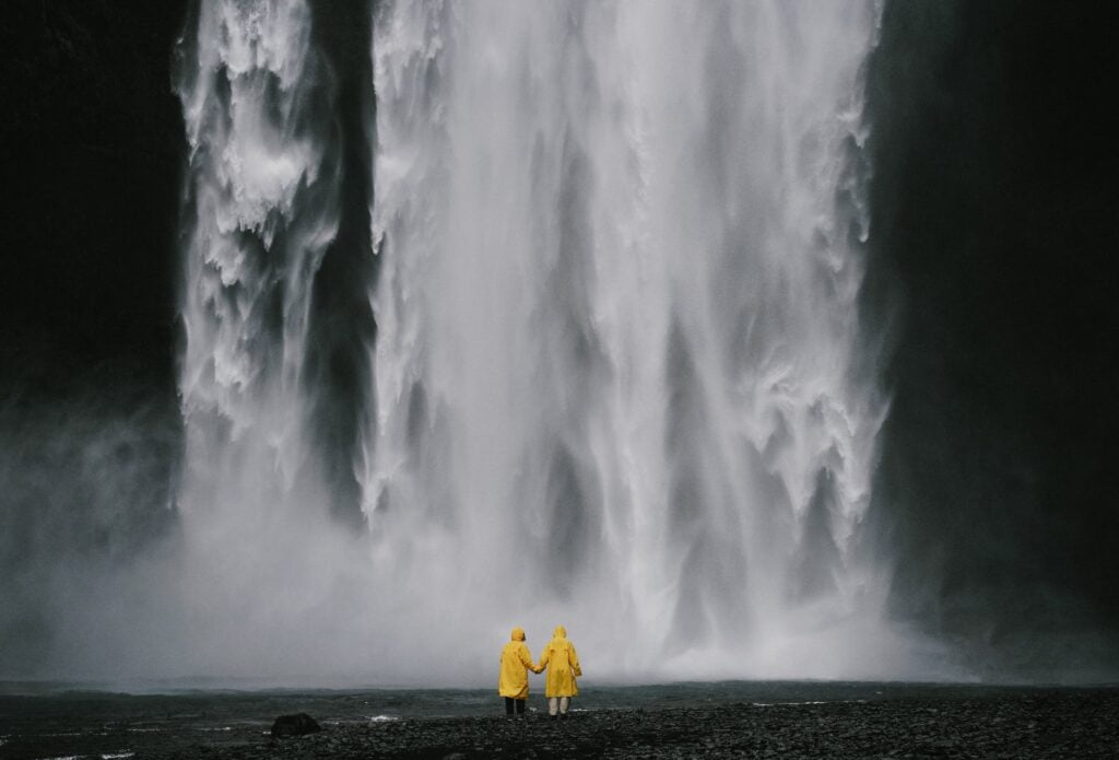 anonymous travelers holding hands against spectacular waterfall, appreciating nature