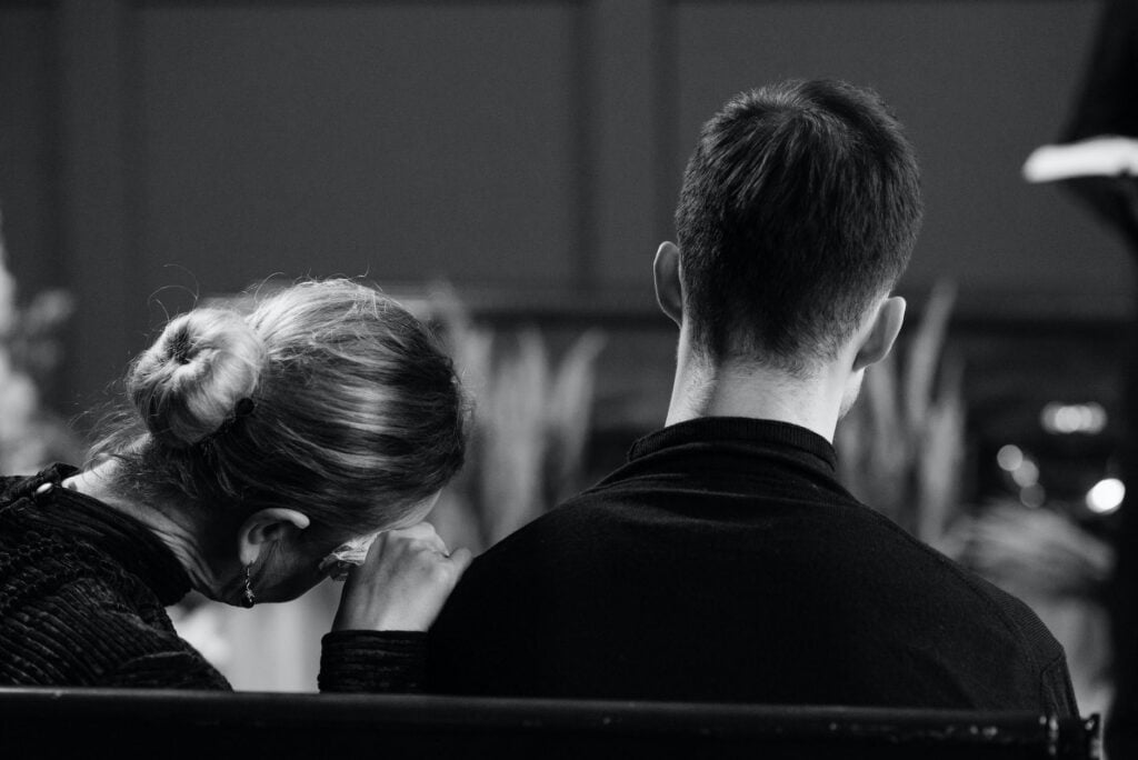 grayscale phot of man and woman sitting on the bench as we talk about how to talk about death