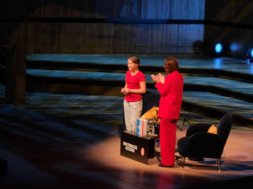 Greta Thunberg quits Edinburgh Book Festival. Activist seen in red T-shirt, standing up on stage as people clap