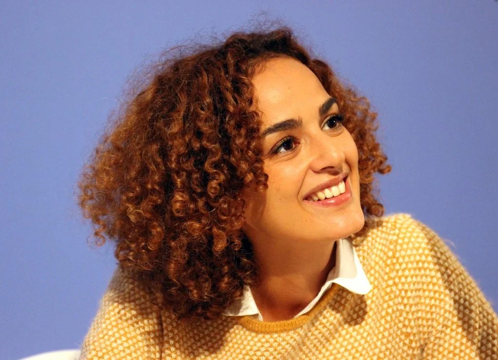 Leila Slimani in yellow jumper and white shirt against a blue background